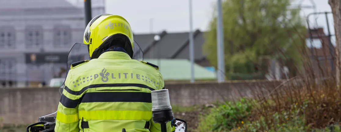 Een politieagent op een motor in een fluorescerend geel-blauw uniform, van achteren gezien langs de weg