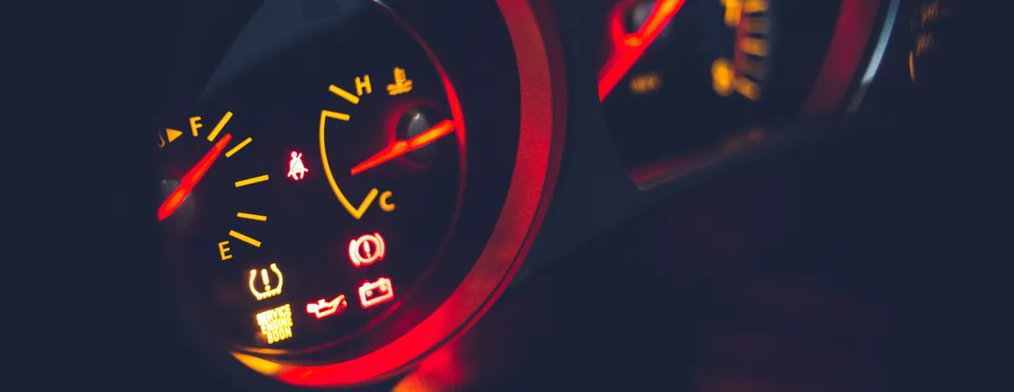 Een verlicht dashboard in het donker met de brandstofmeter, de temperatuurmeter en oranje waarschuwingslampjes