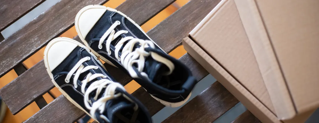 Een paar zwarte sneakers en een kartonnen doos op een houten bankje