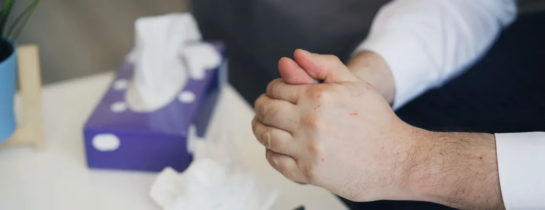 Iemand zit met gevouwen handen aan een tafel, naast een doos tissues en een bril