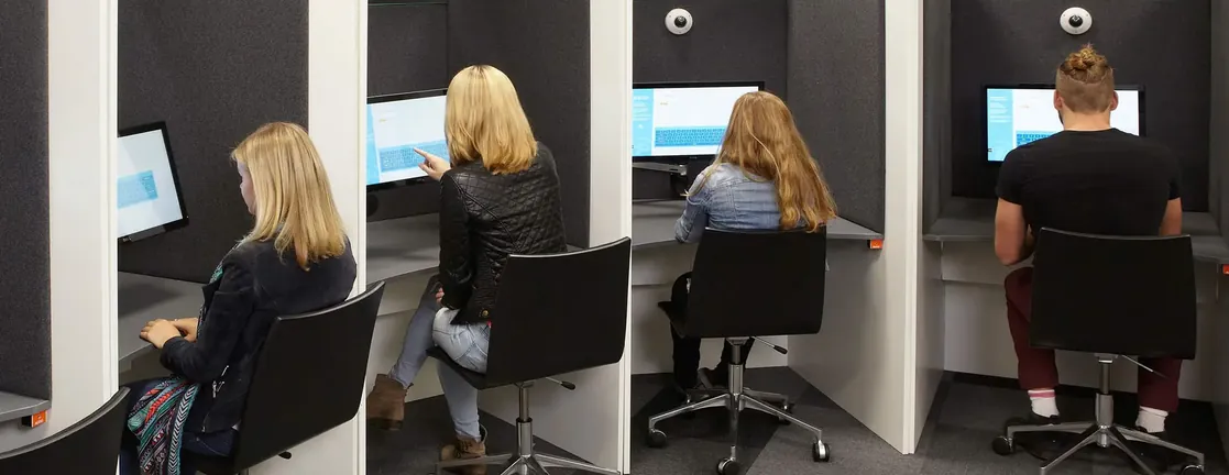 Kandidaten maken het theorie-examen aan computers in genummerde hokjes in een examenzaal van het CBR